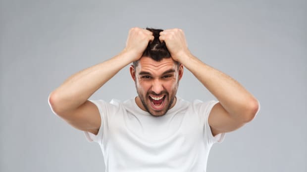 emotions, stress, madness and people concept - crazy shouting man rending ones hair in t-shirt over gray background