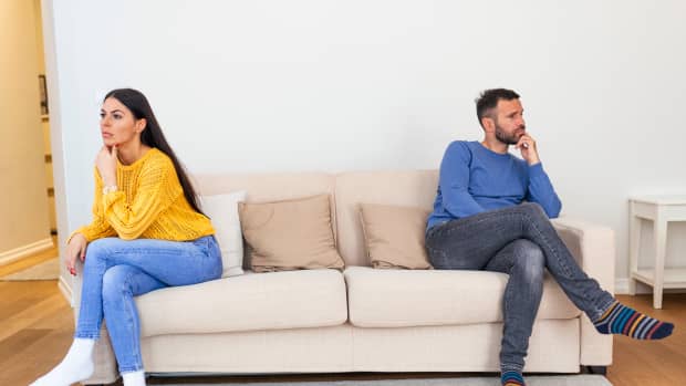 Husband and wife sitting on the couch and not talking after an argument at home. Social Distancing concept
