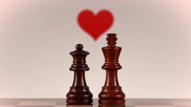 King and Queen in love on an empty chess board with a heart above them and a reflection on the checkered board. This image symbolizes a powerful relationship between two people